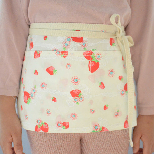 a baby girl wearing a half apron with strawberry prints