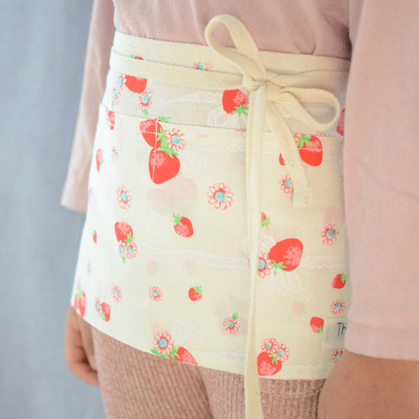 a girl wearing a half apron with strawberry prints on the side view